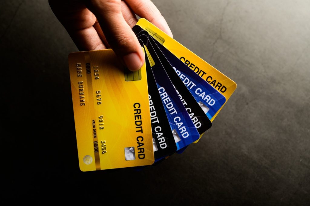 Hand holding several credit cards fanned out, including yellow, blue, and black ones, on a dark surface under soft lighting. The image emphasizes financial variety and consumer credit options. 